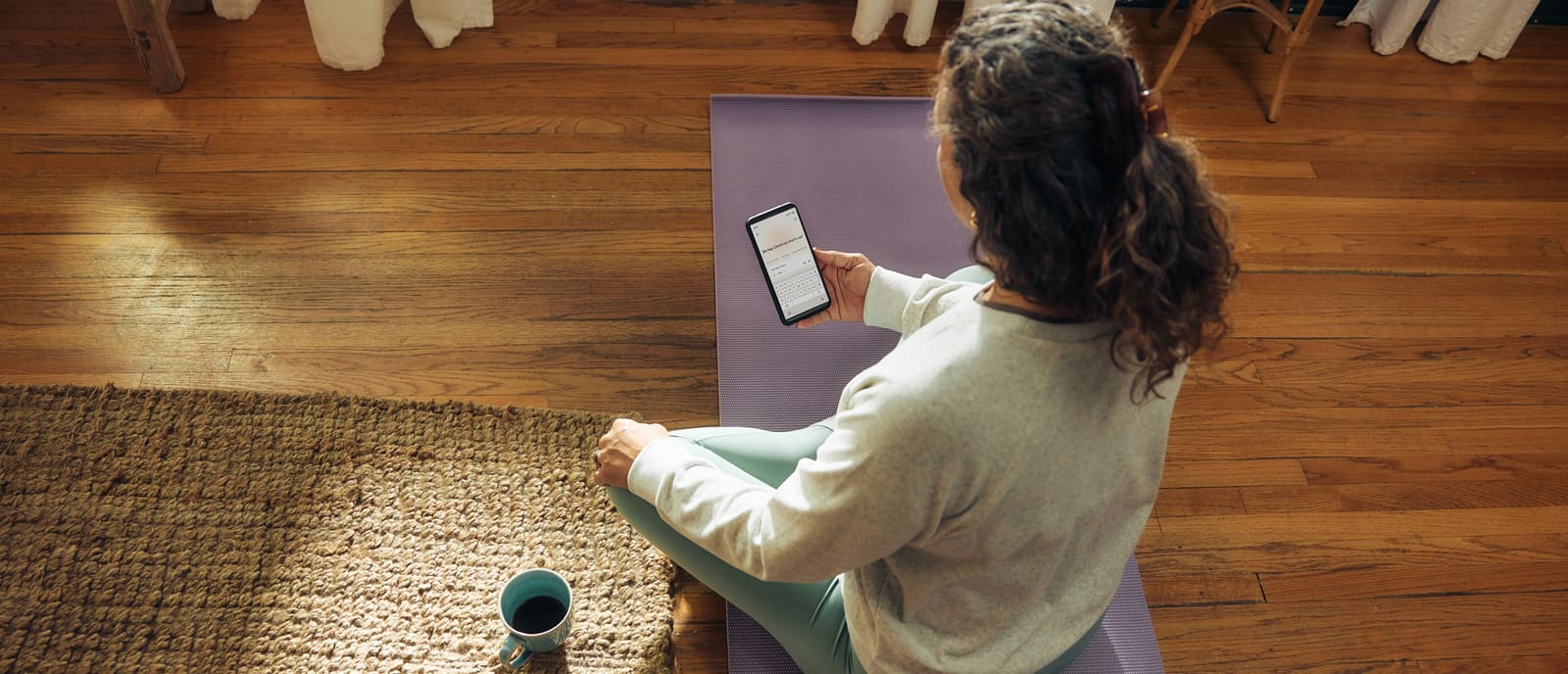 Sitting on a mat at home with a coffee, reading a message on a phone.